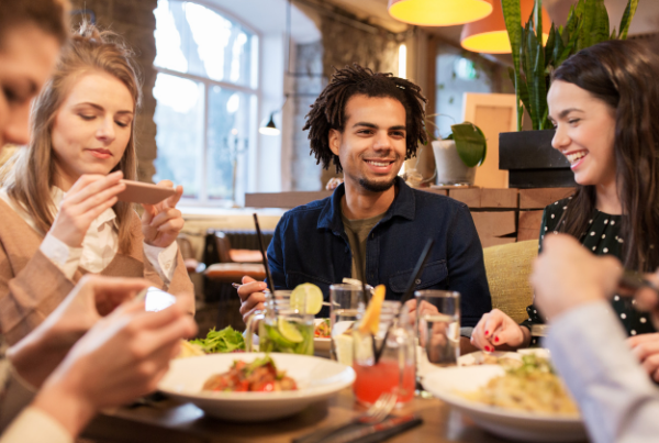 un groupe de 4 personnes avec deux hommes et 3 femmes dînant au restaurant avec le sourire